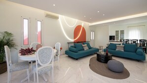 A modern living room with a sofa set, a dining table with chairs, and a kitchen area in the background.