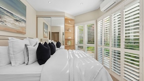 Un dormitorio moderno con una cama grande, un vestidor y vistas a través de persianas blancas.