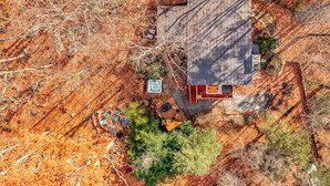 An aerial view of a house with a large deck, surrounded by trees and a dry landscape. - Stone Cabin on Valley View: Fire Pit + Hot Tub (Harpers Ferry)