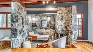 A stone-walled room with a fireplace, a sofa, and a wooden floor. - Stone Cabin on Valley View: Fire Pit + Hot Tub (Harpers Ferry)