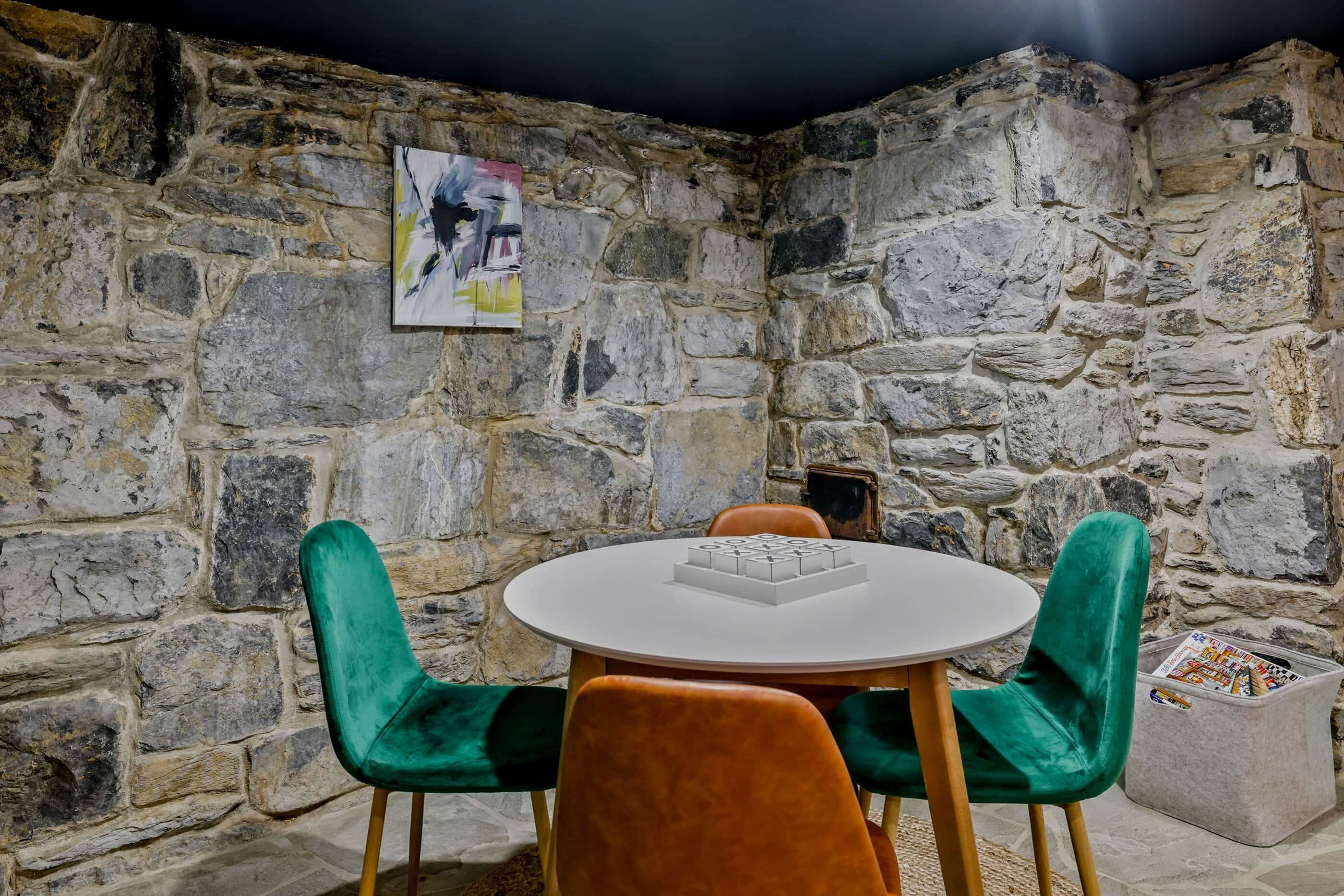 A stone-walled room with a round table and two chairs, one green and one orange.