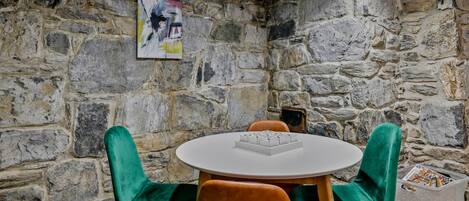 A stone-walled room with a round table and two chairs, one green and one orange.