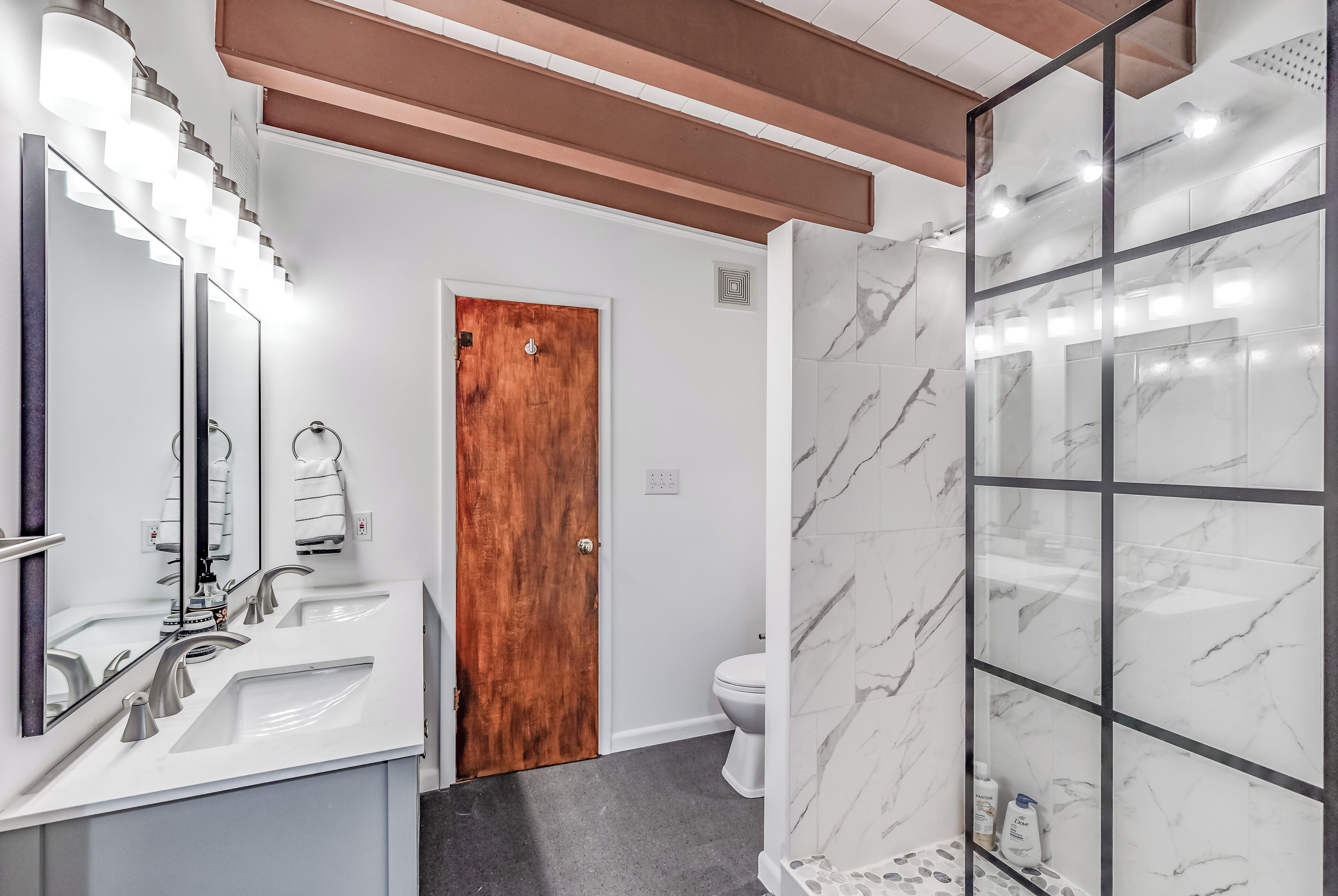 A modern bathroom with a wooden door, a white sink with a mirror, and a glass shower enclosure.
