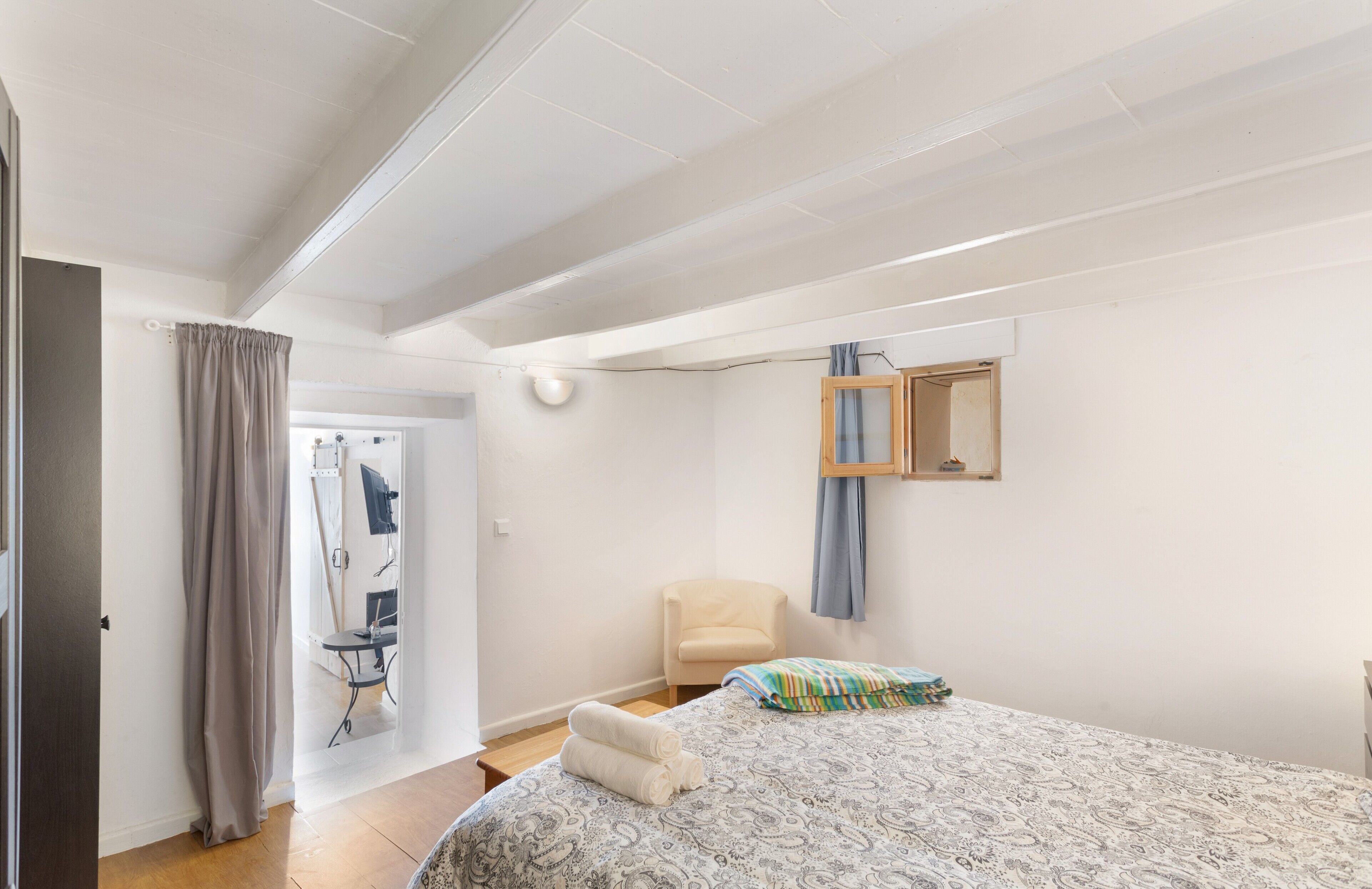 Une chambre à coucher comprenant un lit, une chaise, un miroir et une porte donnant sur une salle de bain.