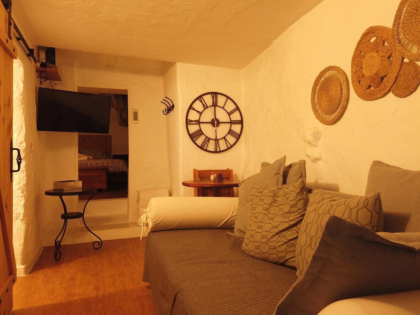 Ein gemütliches Zimmer mit einem Bett, einem kleinen Tisch, einer Wanduhr und einem flachbildfernseher, der an der Wand befestigt ist.