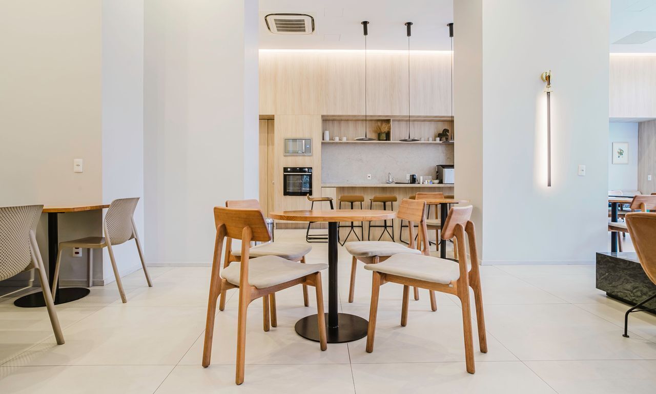 Un comedor moderno con una mesa redonda y sillas, una cocina al fondo y una lámpara colgante.
