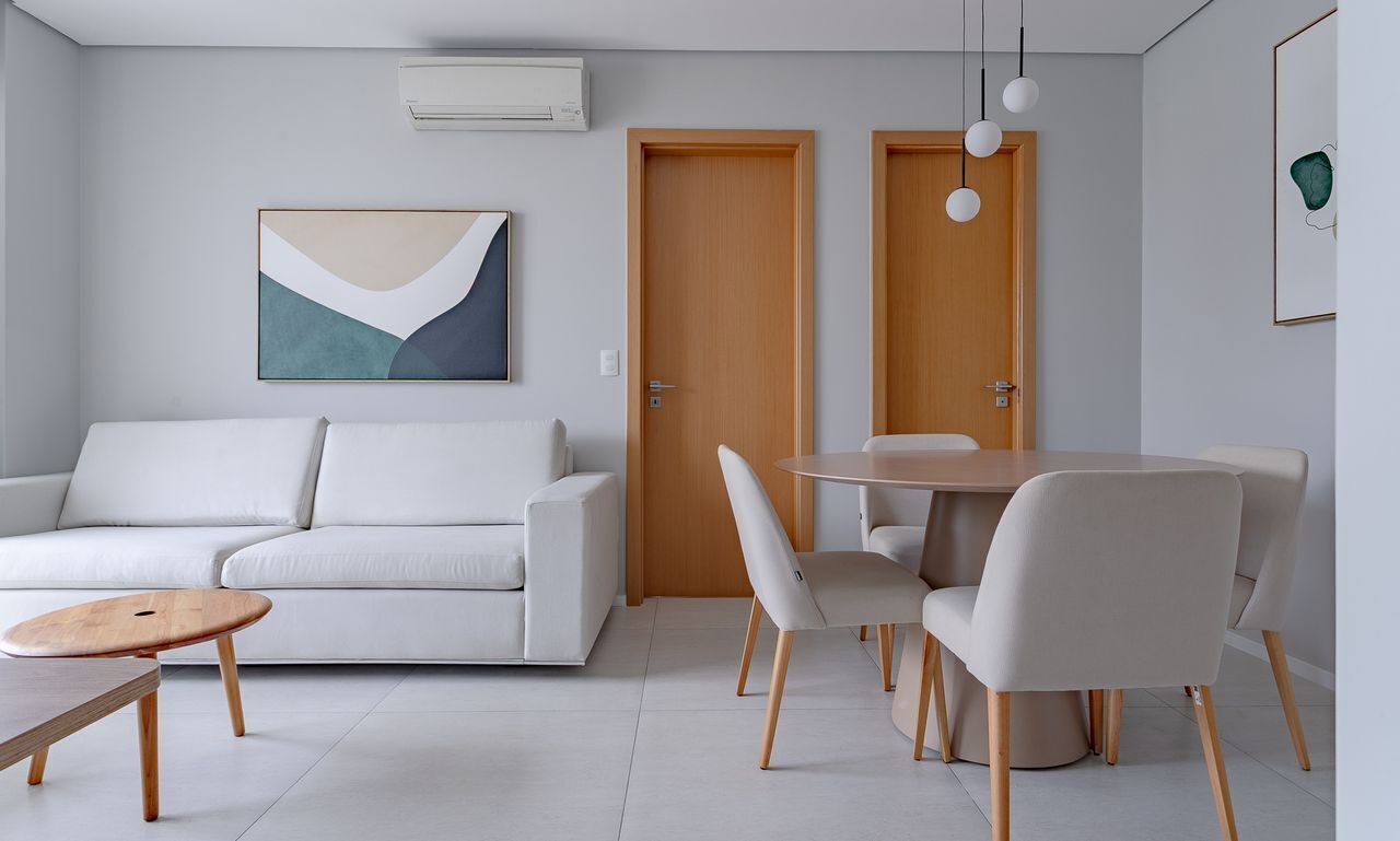Een moderne woonkamer met een bank, een ronde eettafel en stoelen. Er is een houten deur en een lijst met een abstract schilderij aan de muur.