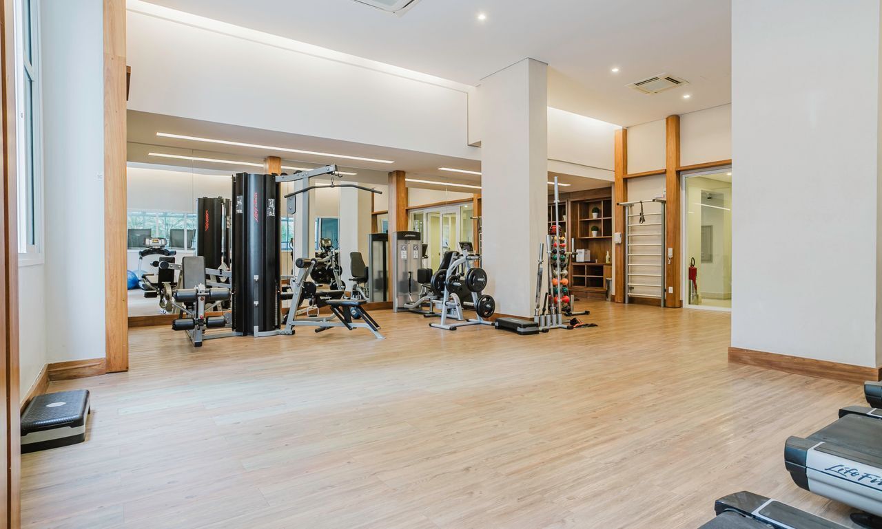 A spacious gym with various exercise equipment, a wooden floor, and a bright interior.
