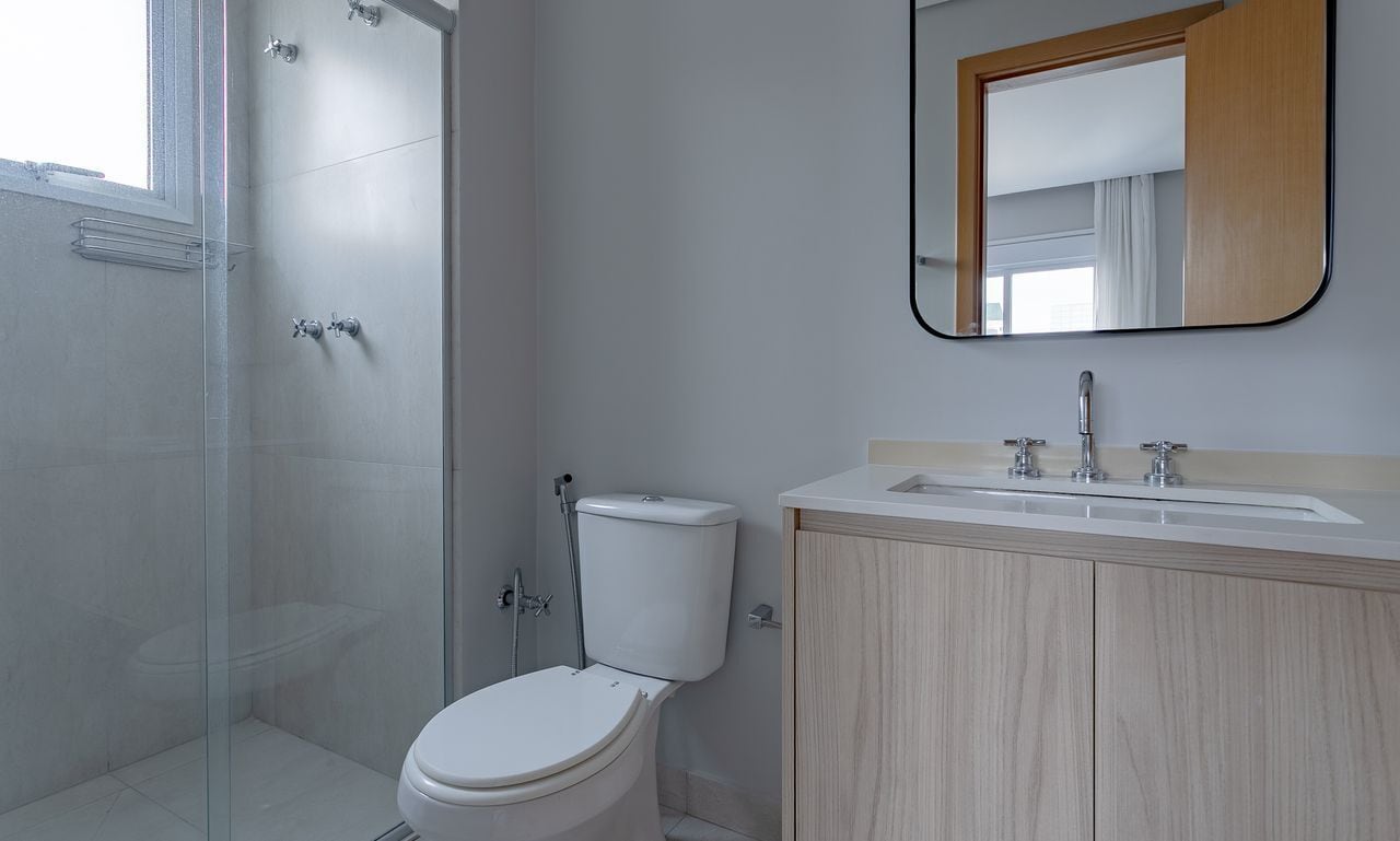 Een moderne badkamer met een douchecabine van glas, een toilet, een wastafel met spiegel en houten kastjes.