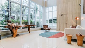 Um quarto espaçoso com amplas janelas, uma mesa de centro de madeira, um sofá branco e um tapete redondo.