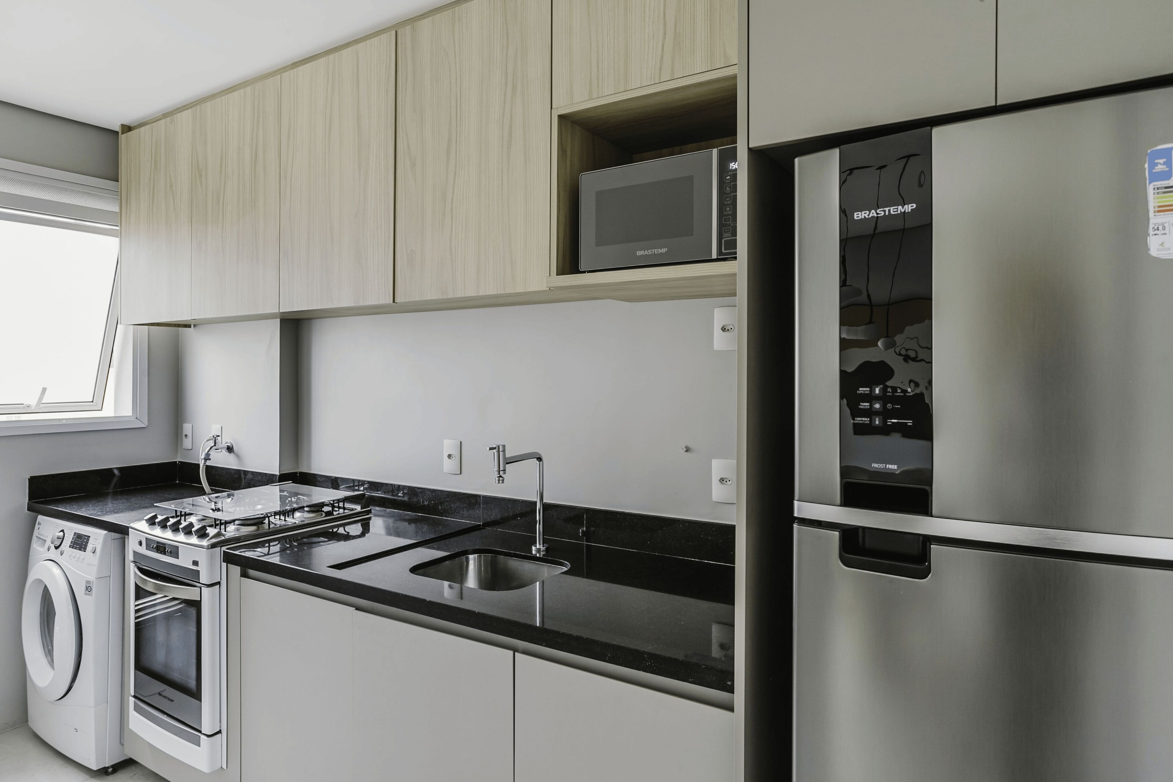 A modern kitchen with a stainless steel refrigerator, built-in microwave, oven, and washing machine.