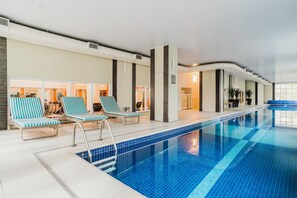 An indoor swimming pool with blue tiles, lounge chairs, and a modern interior design. - Tabas - GO 850 Building in Vila Olímpia (São Paulo)