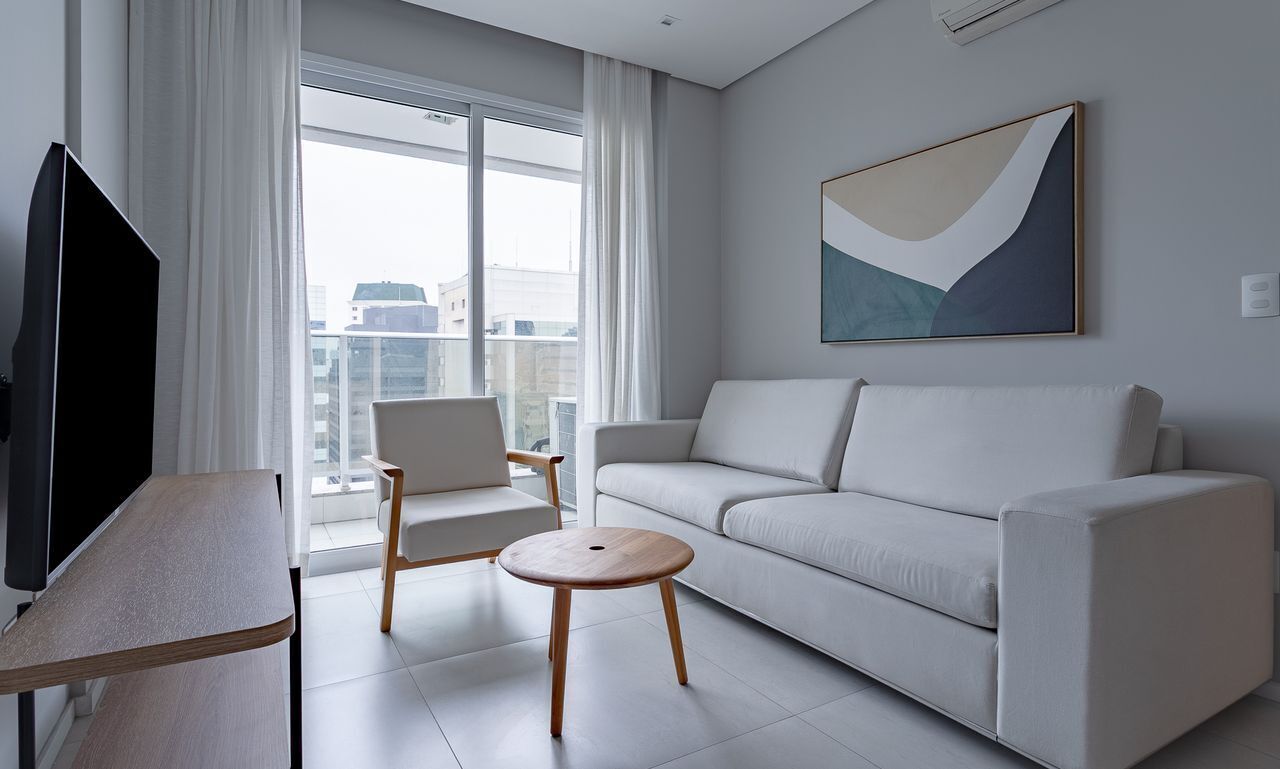 A modern living room with a sofa, a chair, a small round table, a TV, and a large window with curtains.