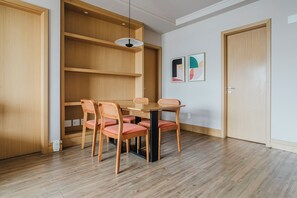 A dining area with a wooden table and chairs, a pendant light, and a wall-mounted shelf. - Tabas - GO 850 Building in Vila Olímpia (São Paulo)