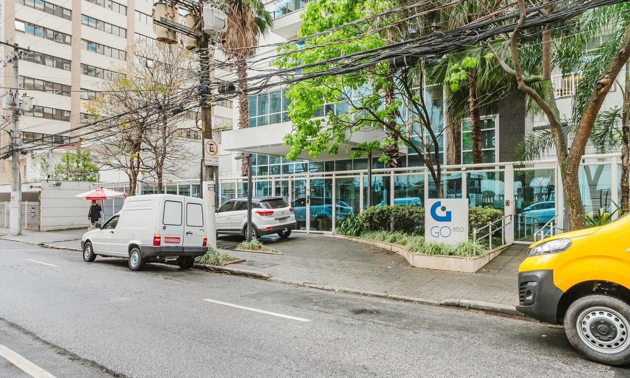 A building with a glass facade, a sign with a blue logo, and a yellow car parked in front.