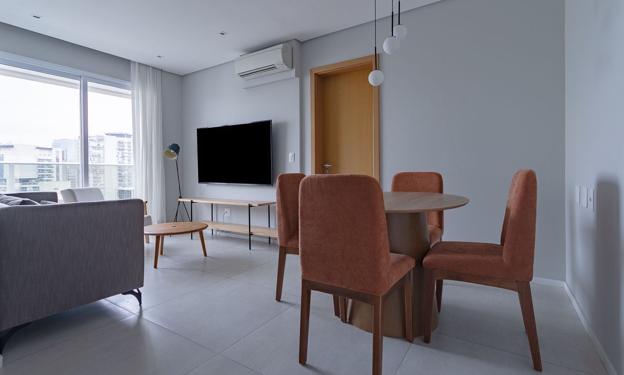 Un salon moderne comprenant un canapé, une table à manger avec des chaises, un téléviseur à écran plat et une grande fenêtre donnant sur la ville.