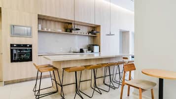 Cozinha moderna com forno embutido, micro-ondas e máquina de café. Há banquetas e uma mesa de madeira.