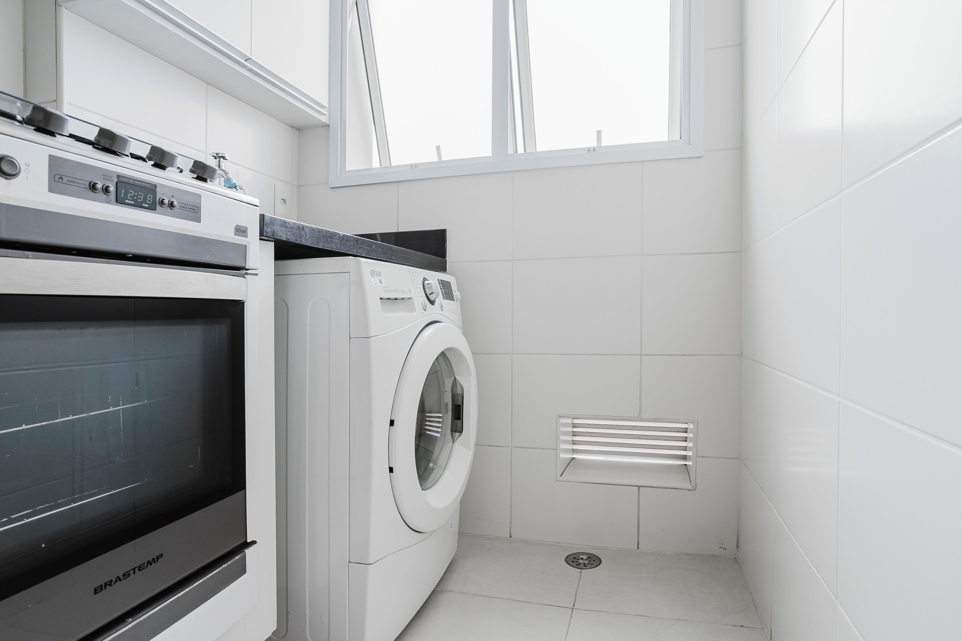 A modern laundry room with a Brastemp washing machine, a dryer, and a stove.