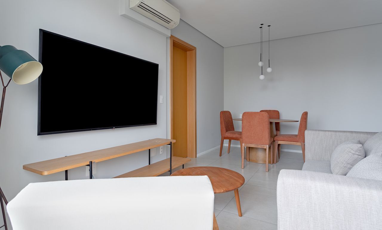 A modern living room with a flat-screen TV, a sofa, a dining table with chairs, a lamp, and an air conditioning unit.