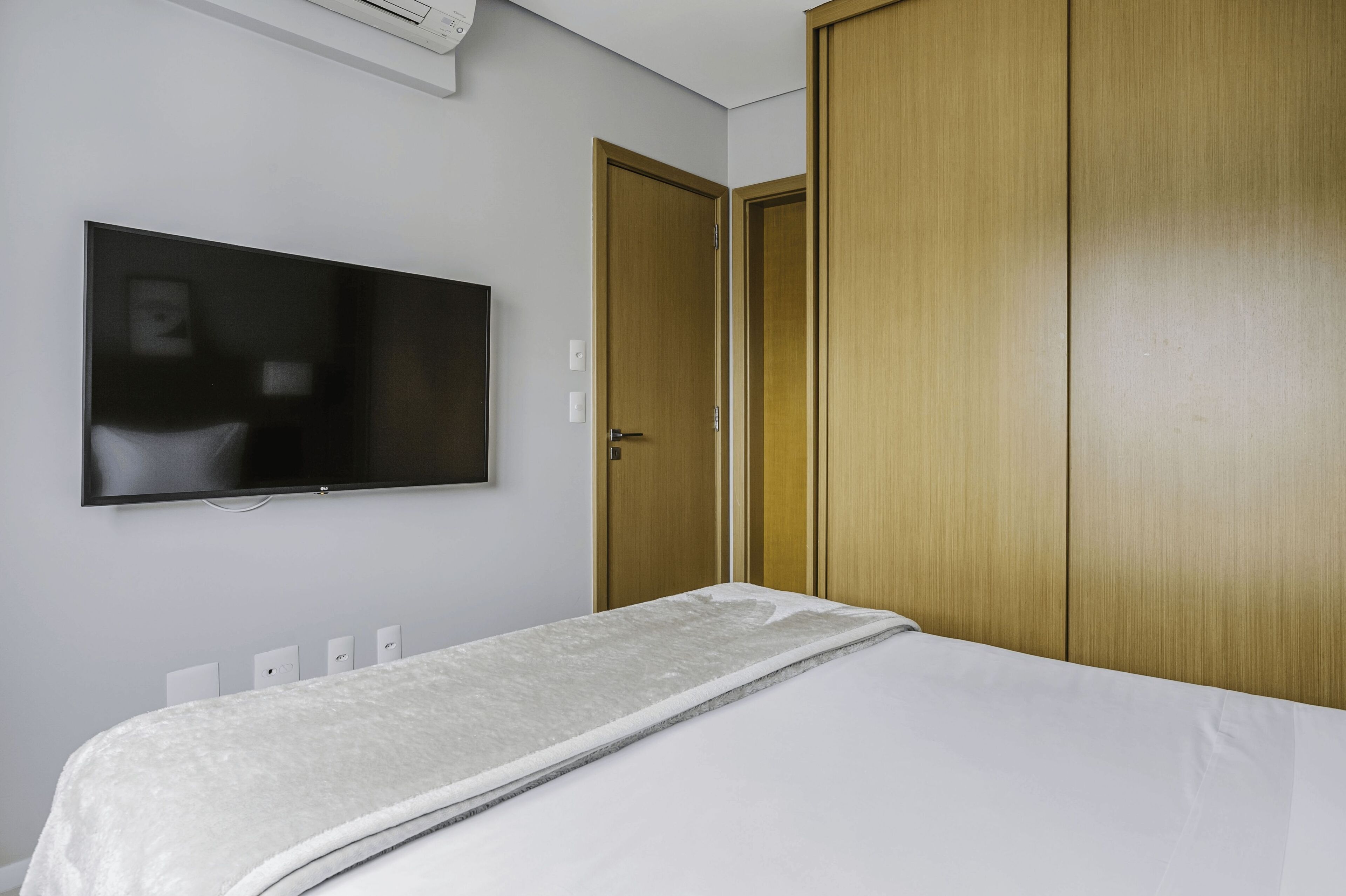Une chambre à coucher avec un lit, un téléviseur fixé au mur et des armoires en bois.