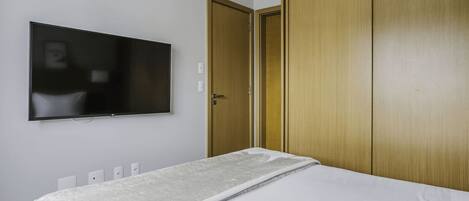 Une chambre à coucher avec un lit, un téléviseur fixé au mur et des armoires en bois.