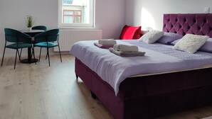 Een slaapkamer met een bed, een raam, een eettafel met stoelen en een radiator.