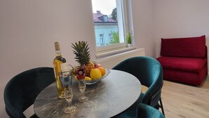 Een eetgedeelte met een ronde tafel, twee stoelen, een fles wijn, een glas en een schaal fruit.