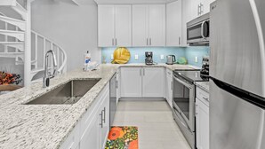 A modern kitchen with white cabinets, stainless steel appliances, a granite countertop, and a blue backsplash.
