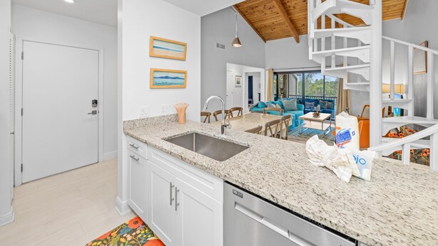A kitchen with granite countertops, a stainless steel sink, and a dishwasher. There is a dining area with a table and chairs, and a staircase with a wooden finish.