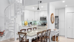 A modern kitchen with white cabinetry, a central island with seating, a stainless steel refrigerator, and a white spiral staircase.