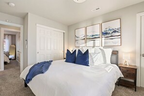 A bedroom with a large bed, a nightstand with a lamp, and artwork on the wall.