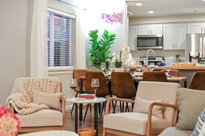 A modern living room with a sofa, chairs, a dining table with wine glasses, and a kitchen in the background.