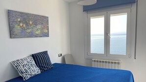 Un dormitorio con cama, ventana con vista al mar y un cuadro en la pared.