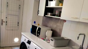 Une cuisine de taille réduite, équipée d’un lave-linge, d’un évier et d’un petit plan de travail.