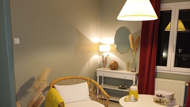 Une pièce chaleureuse avec un fauteuil en osier, une table ronde et une lampe suspendue.