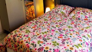 Une chambre à coucher avec un lit recouvert d’une couette à motifs floraux, une armoire avec un miroir et une lampe de chevet.
