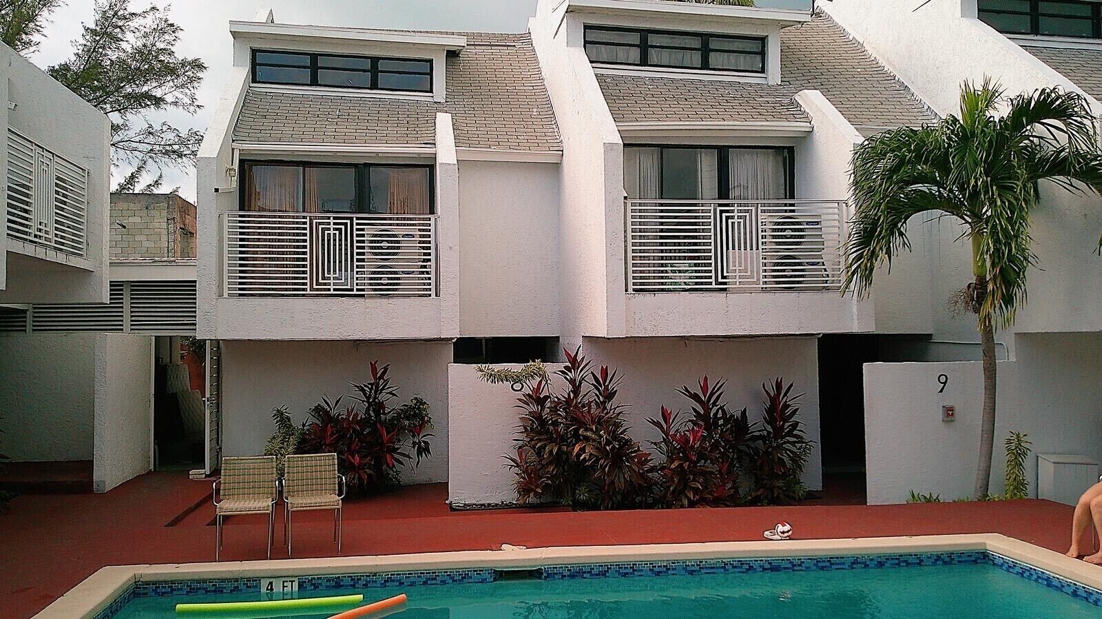 Un edificio de dos pisos con piscina, mesas al aire libre y un letrero con el número 9.