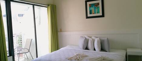 A hotel room with a bed, pillows, a framed picture on the wall, and a balcony with a chair.