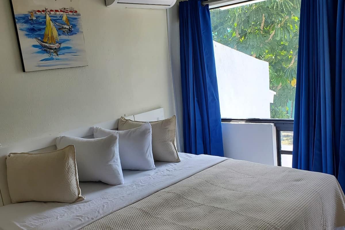 Habitación de hotel con cama, almohadas, un cuadro, aire acondicionado y ventana con cortinas.