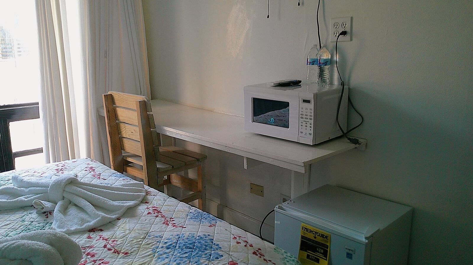 Une chambre d’hôtel équipée d’un lit, d’une chaise en bois, d’un four à micro-ondes et d’un petit réfrigérateur.