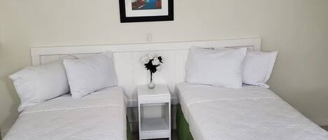 Una habitación con dos camas individuales, una mesita de noche, un ventilador de techo y un cuadro en la pared.