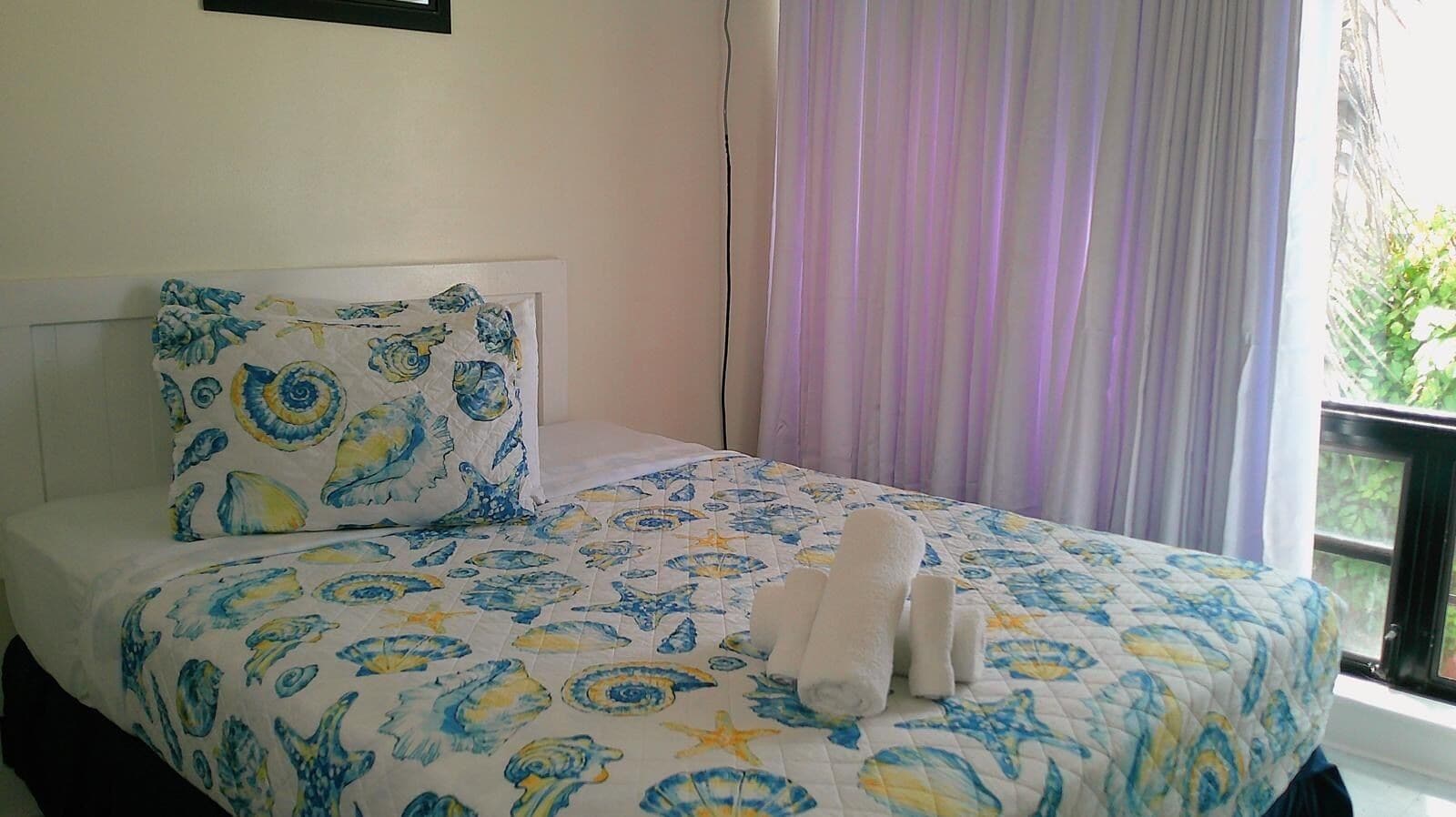 Una cama con colcha y almohada de motivos florales en azul y amarillo, y dos toallas enrolladas.