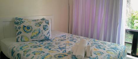 Una cama con colcha y almohada de motivos florales en azul y amarillo, y dos toallas enrolladas.