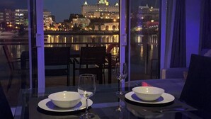 Una mesa de comedor con dos cuencos y copas de vino, con vistas a un paisaje urbano con edificios iluminados por la noche.