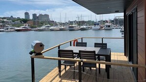 Terraza de madera con mesa y sillas que da a un puerto deportivo con barcos.