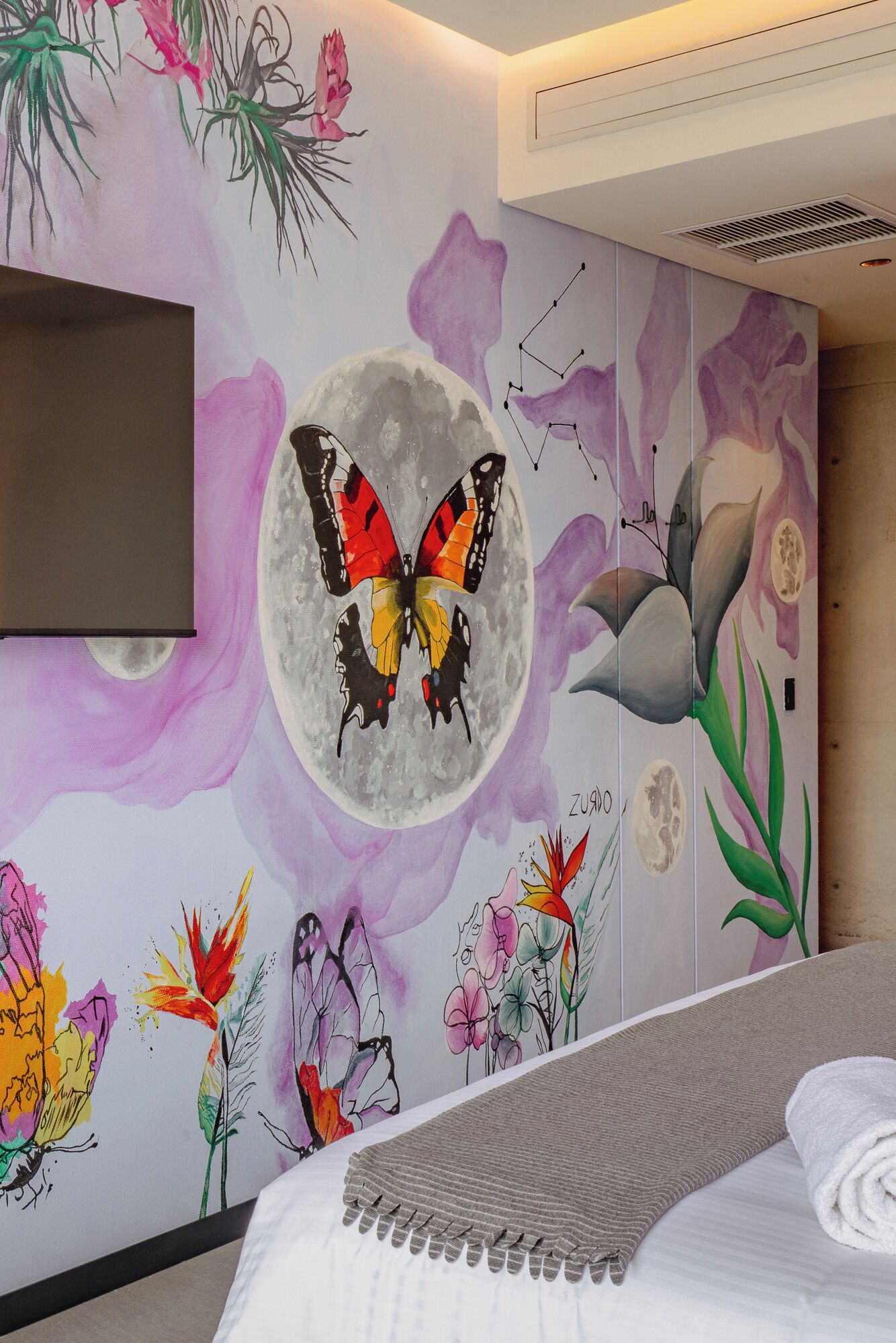 A bedroom with a bed, a wall-mounted TV, and a decorative wall with a butterfly and floral designs.