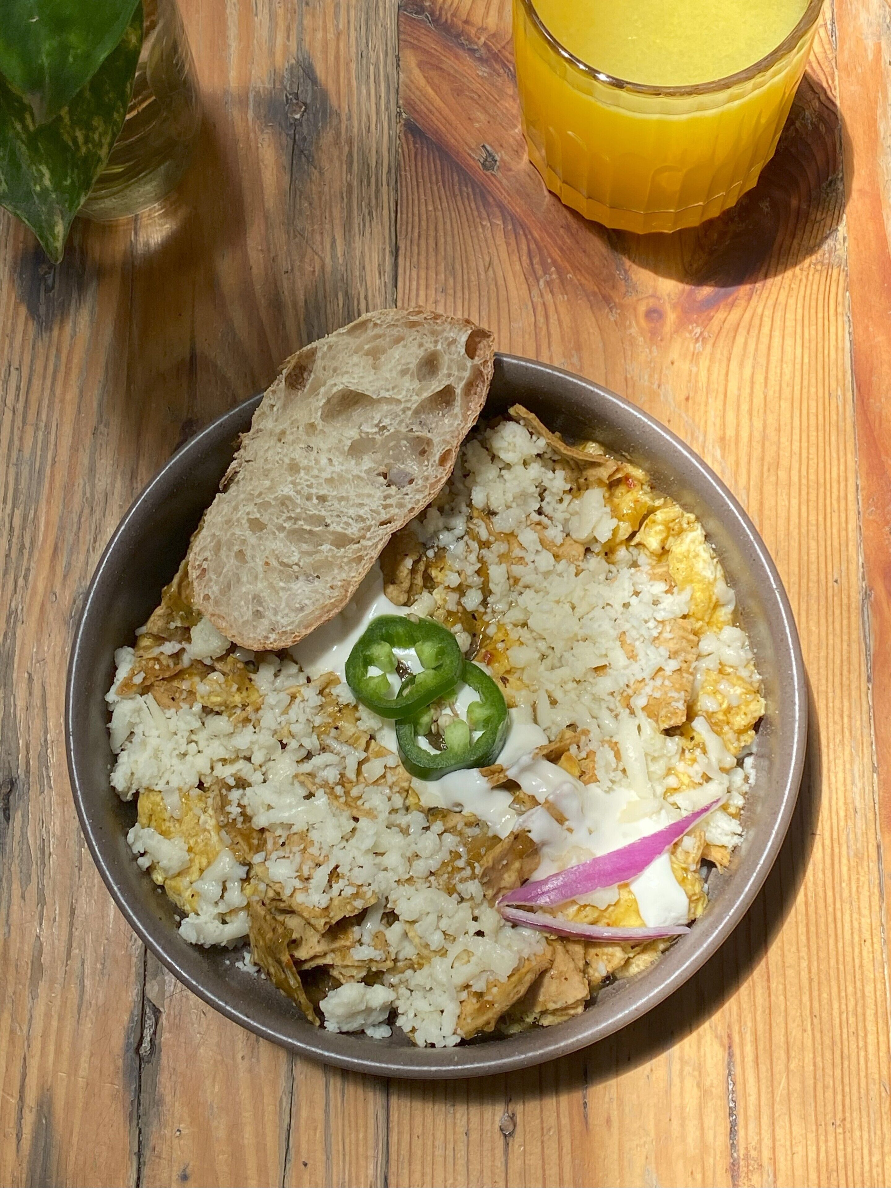 A meal with rice, eggs, and vegetables on a plate, accompanied by a slice of bread and a glass of orange juice on a wooden table.