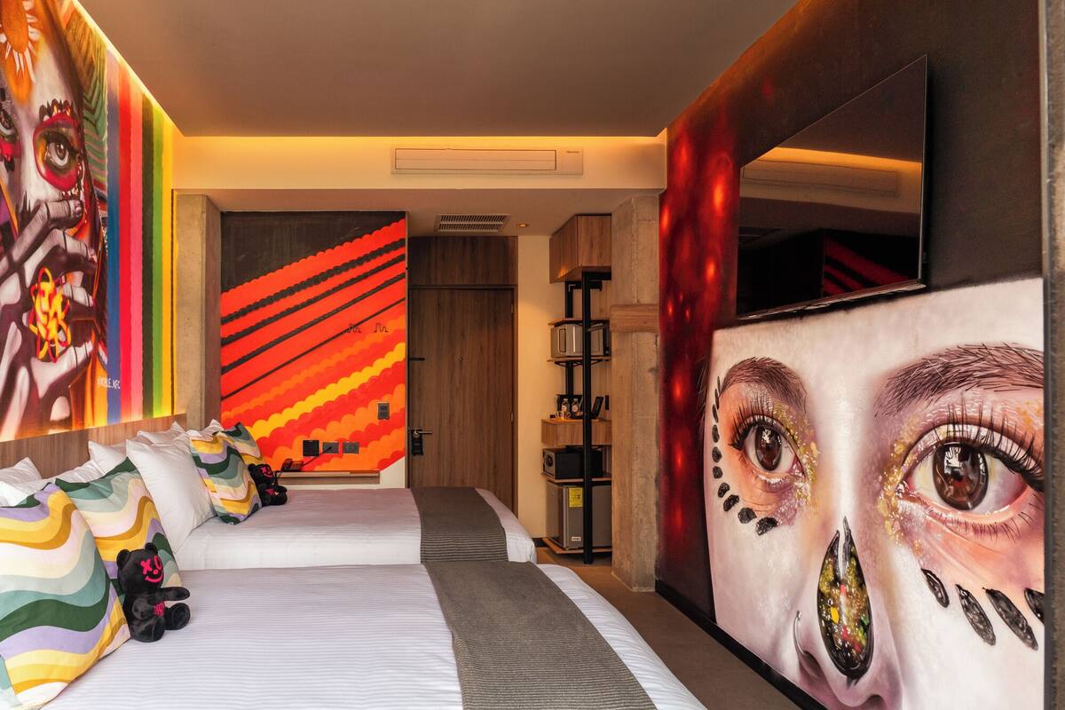 A hotel room with two beds, a large mirror, and colorful artwork on the walls.