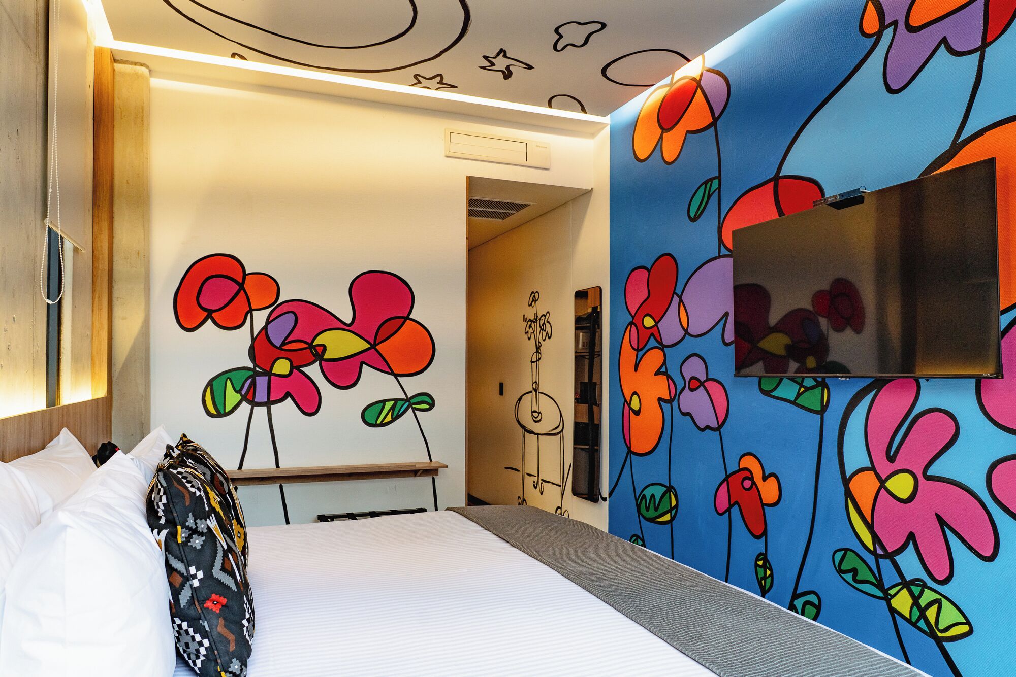 A hotel room with a bed, a mirror, and a wall with colorful floral patterns.