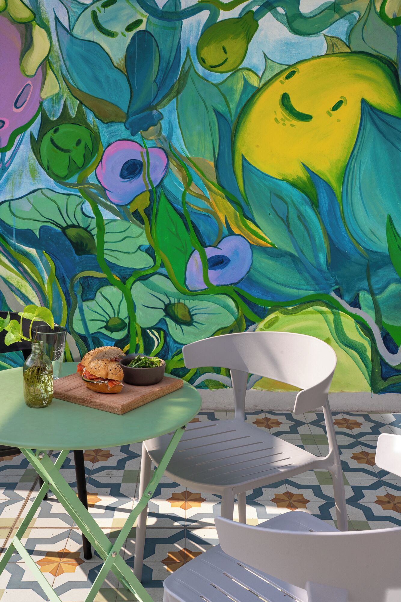 A dining area with a table set for two, a chair, and a colorful mural on the wall.